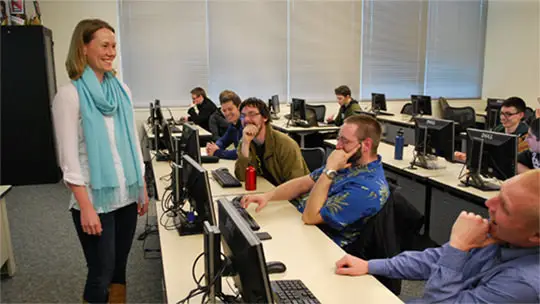 Grado Asociado en Ciencias de la Computación Estudiantes en un aula de laboratorio de computación prestando atención al instructor al frente del aula