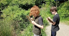 Two children writing on notebooks outside
