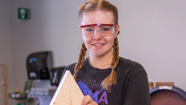A girl in googles building a birdhouse