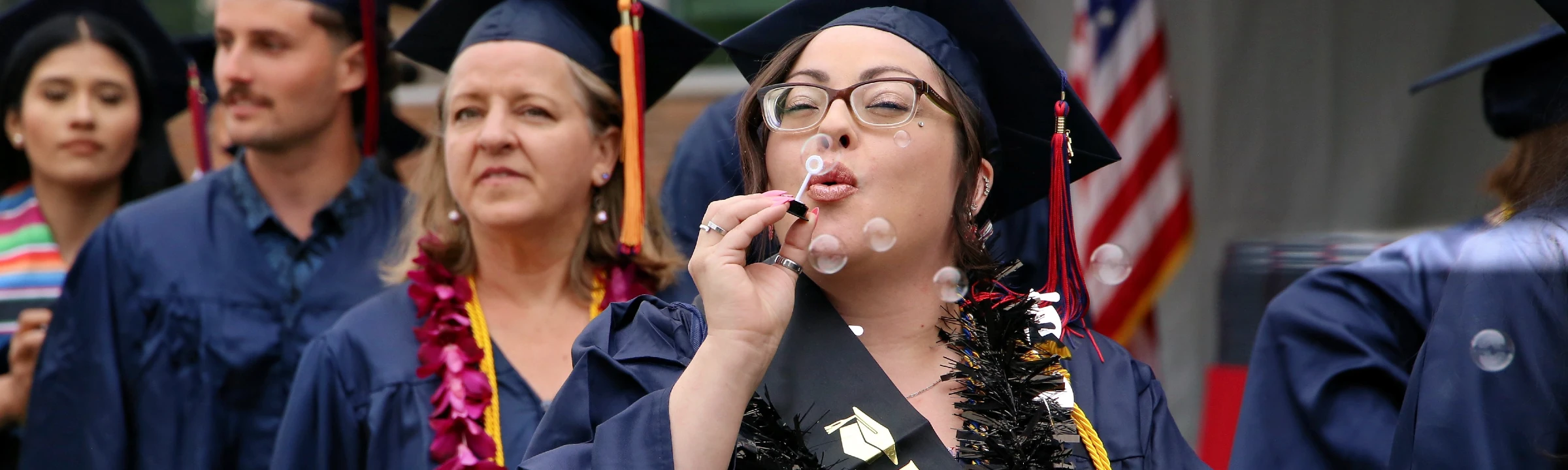 CCC graduates lined up in caps and gowns during the commencement ceremony. The graduate in the foreground is blowing bubbles.