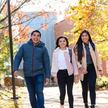 A group of students walks between buildings on campus with fall foliage in the background