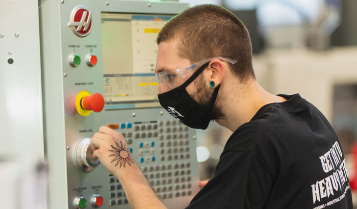 CCC student with mask on operating a CNC machine