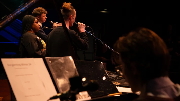 CCC concert photo of a pianist and three vocalists shown from perspective behind stage