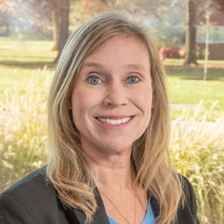 Beth Wicklund smiling, outdoors in a landscaped campus setting.