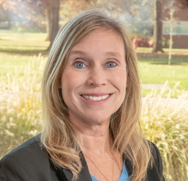 Beth Wicklund smiling, outdoors in a landscaped campus setting.