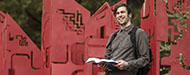 student holding open book stands near sculpture on Oregon City campus