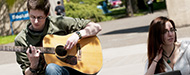 Two students outside in the quad on Oregon City campus. One is playing a guitar.